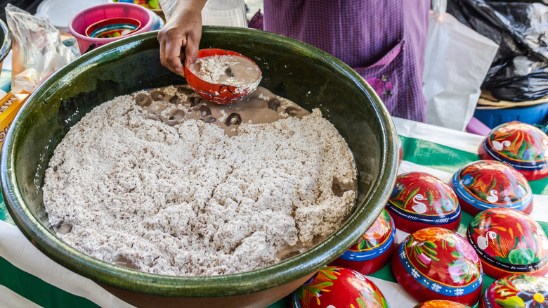 A person filling a cup of tejate from a giant bowl at a market in Oaxaca