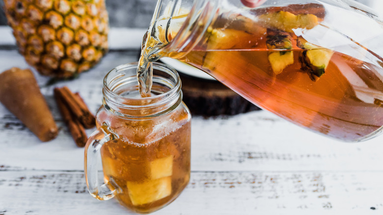 A person pouring tepache pineapple drink into a glass