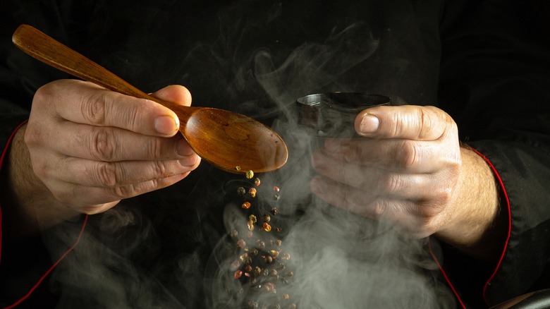 hands adding peppercorns to food