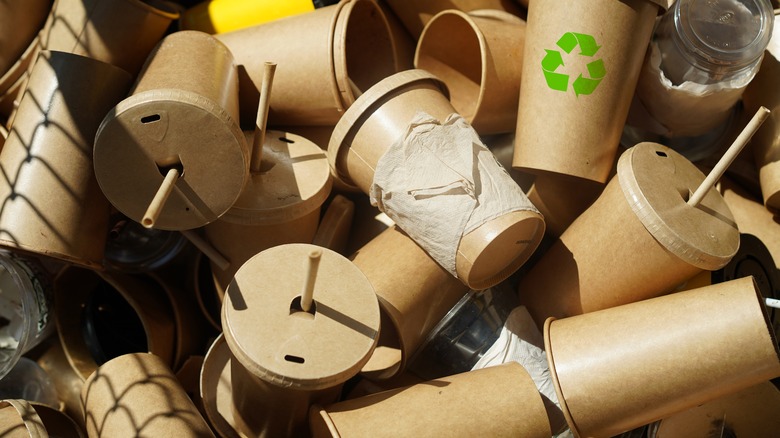 large pile of brown paper cups with lids and straws