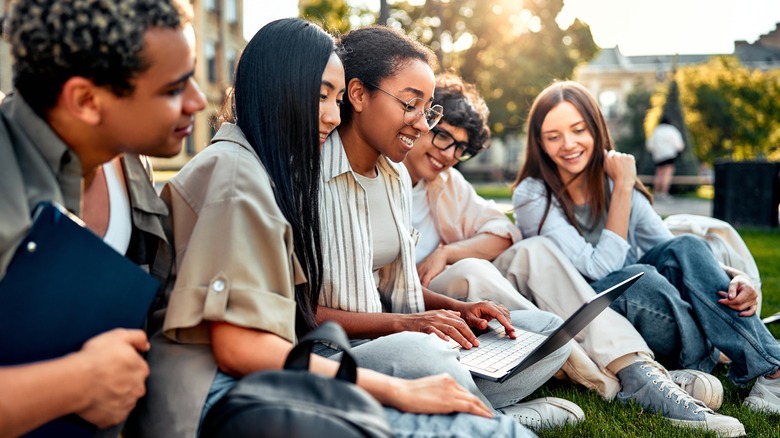 young people with a laptop sitting outside on a college campus