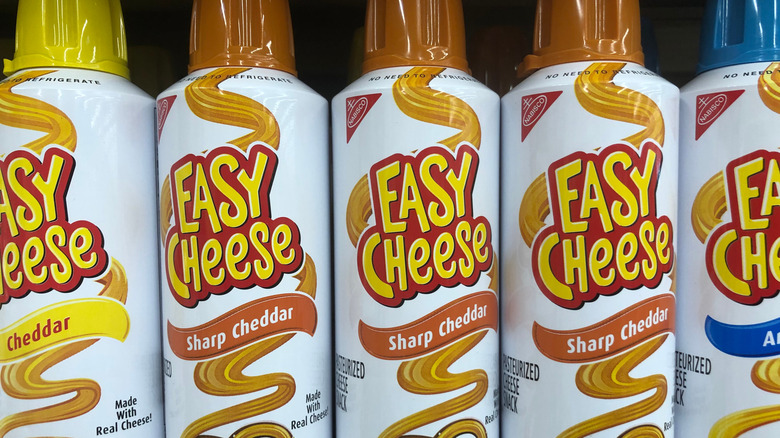 Cans of Easy Cheese spray cheese on a shelf at a grocery store