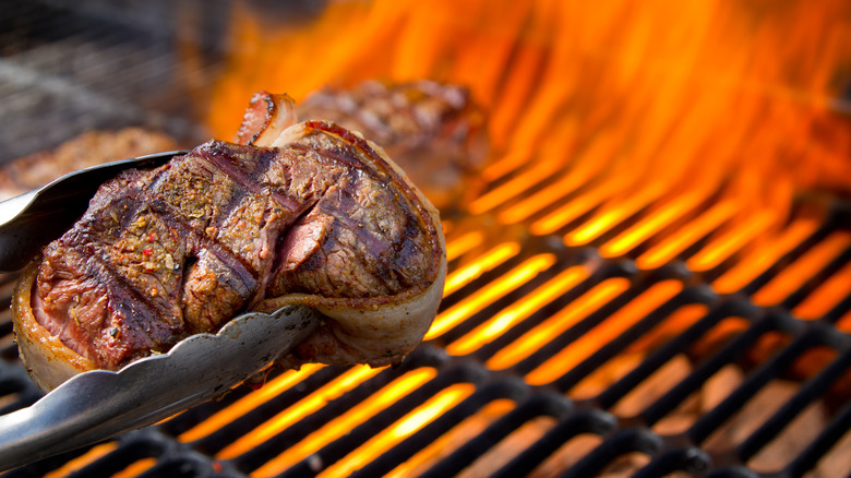 Tongs holding seared steak over grill