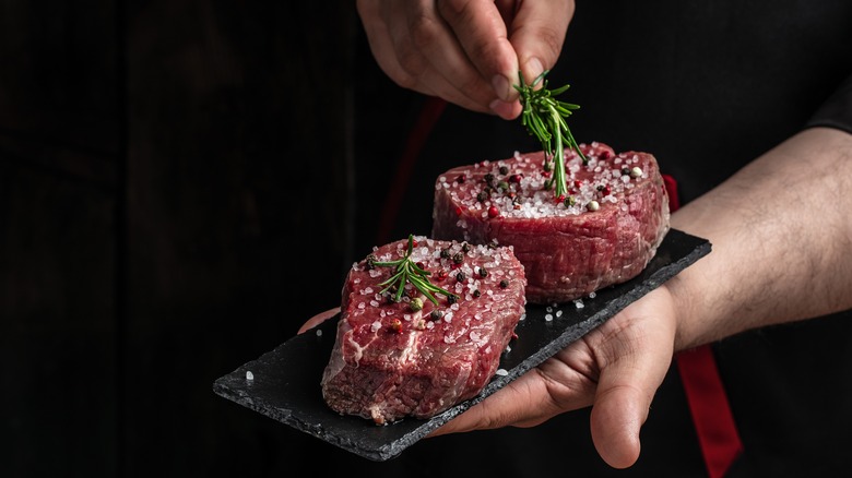 Person holding seasoned raw steaks