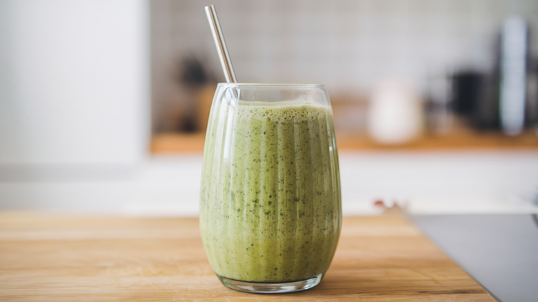 A green smoothie in a glass on a wooden cutting board
