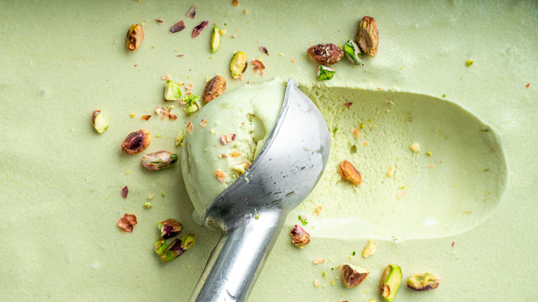 An ice cream scoop picking up pistachio ice cream