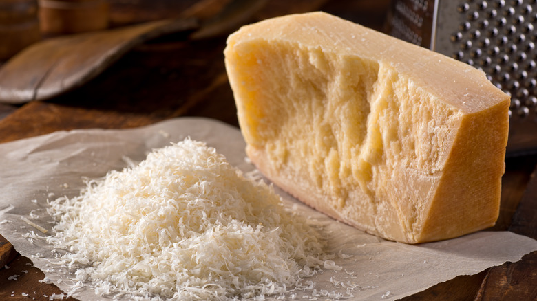 A chunk of Parmesan cheese next to shredded Parmesan cheese on parchment paper
