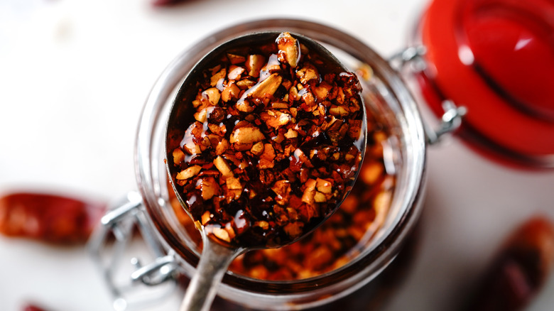 Chili crisp in a glass jar underneath a spoonful of chili crisp