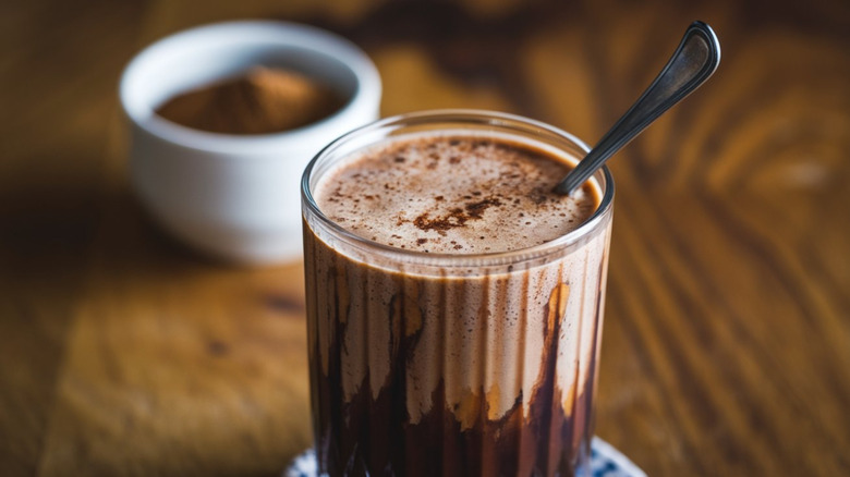 Malted milkshake in a glass with a spoon in front of a bowl of malted milk powder