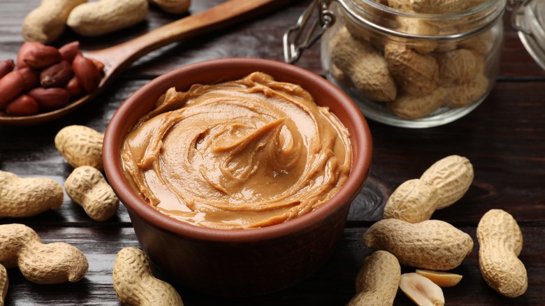 A small bowl of peanut butter surrounded by shelled and whole peanuts