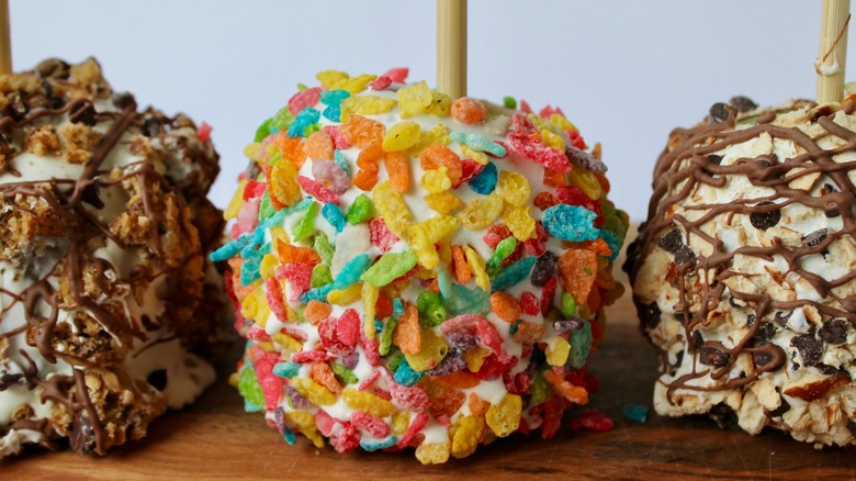 Three candy apples coated with colorful cereal, chocolate chips, and chocolate