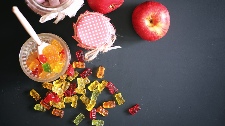 A jar of gummy candies next to an apple