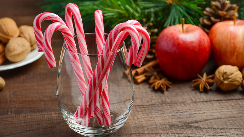 Candy canes in a glass with two apples and nuts in the background