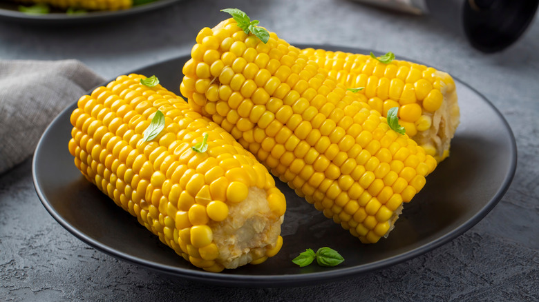 Three small corn cobs on a black plate
