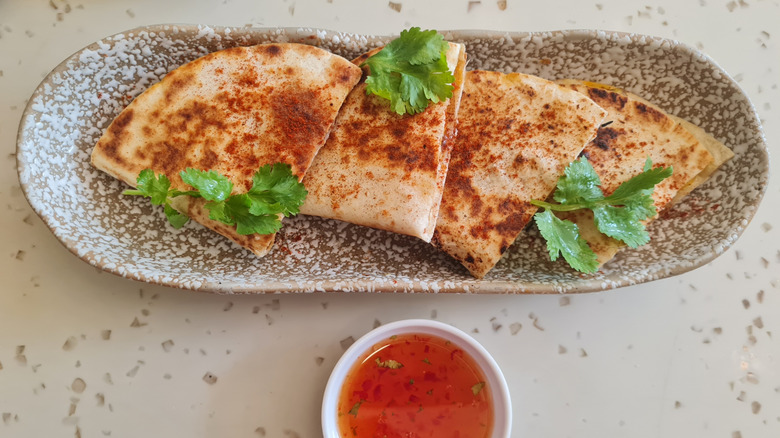 A quesadilla on a skinny plate with dip below