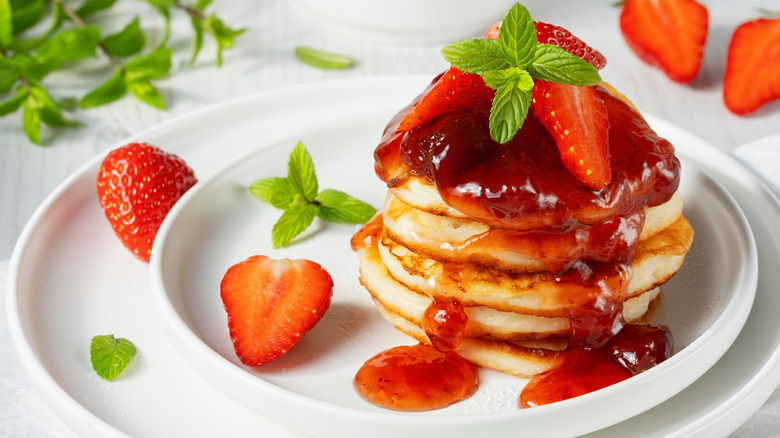 A stack of mini pancakes covered in strawberries and syrup