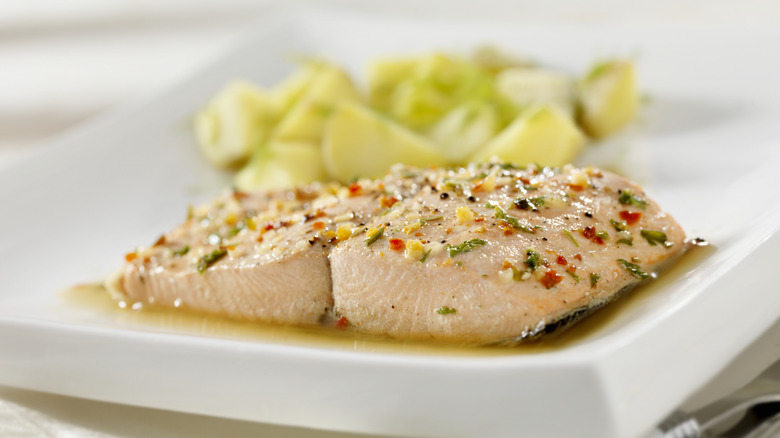 Poached salmon on a plate with veggies behind it
