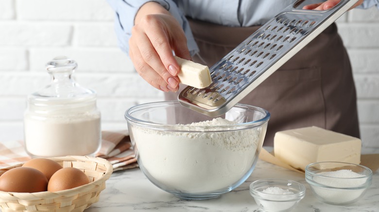 Person grating butter into bowl of flour