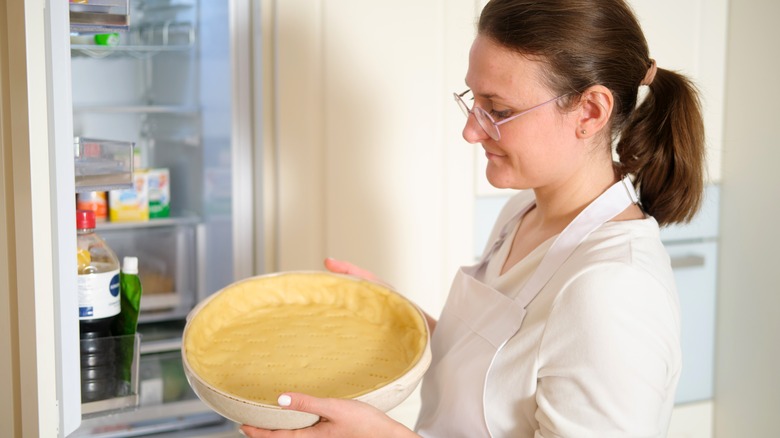 Woman removing dish with pie dough from refrigerator