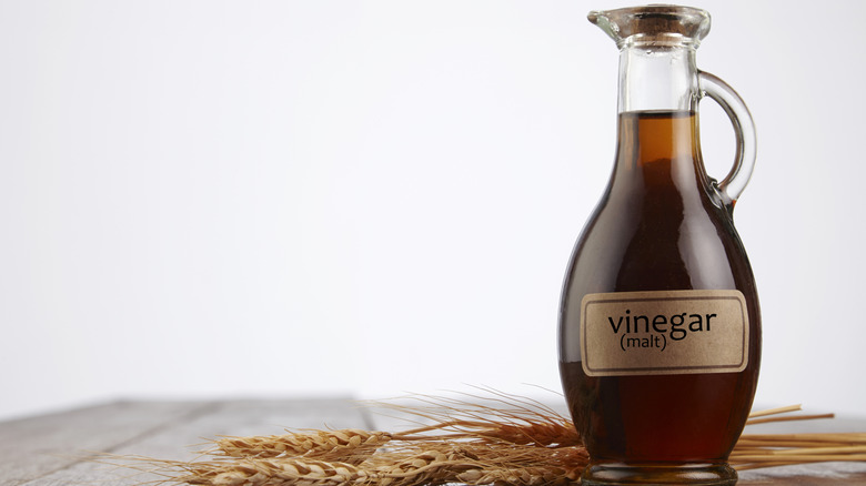 bottle of malt vinegar on wooden table with wheat