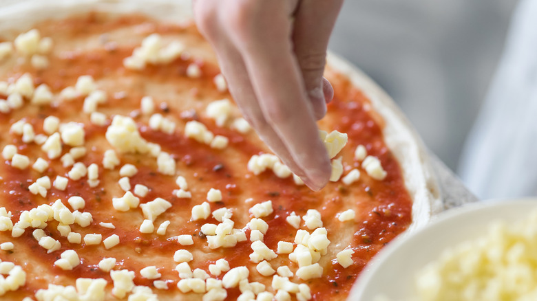 hands putting cheese on pizza