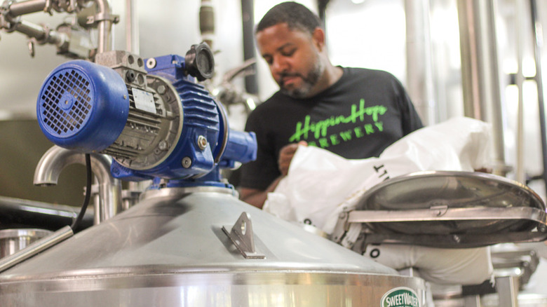 A person pouring ingredients into a beer barrel