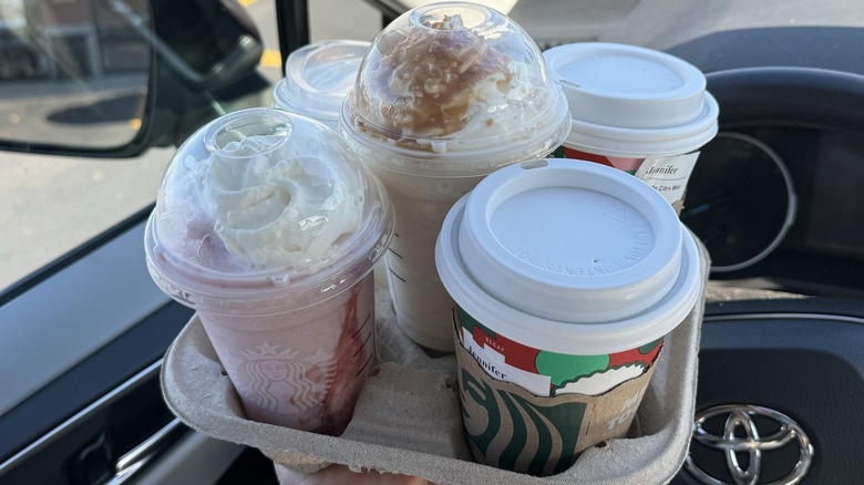 Various Starbucks drinks sitting in a cup holder inside a car