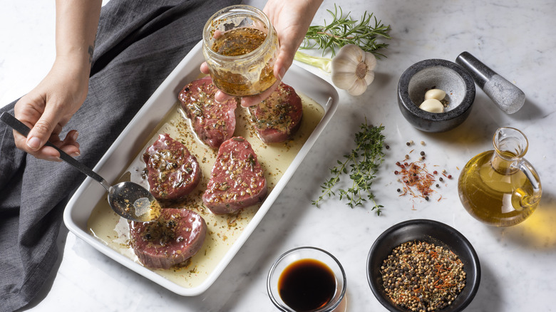 A person spooning marinade onto raw steaks