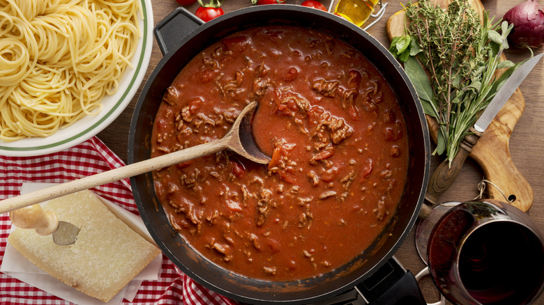 A pot of bolognese sauce next to a bowl of pasta and sauce ingredients