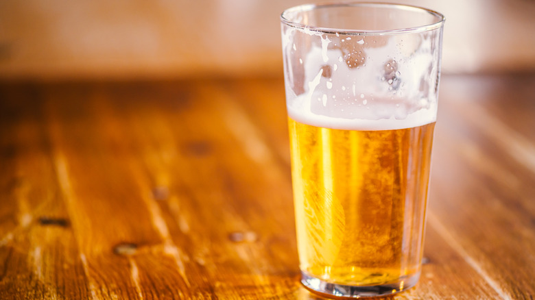 A half-full glass of beer on a wooden countertop