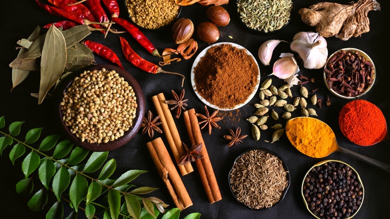 Small bowls of spices sit together with whole ingredients nearby