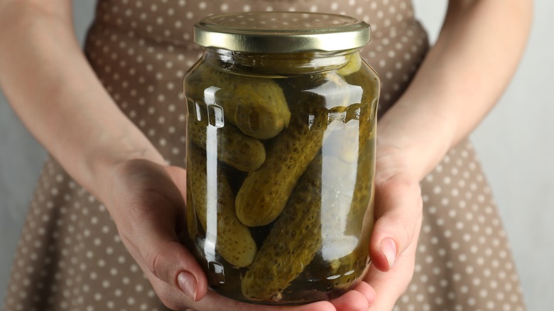 A woman holds a jar of whole pickled cucumbers