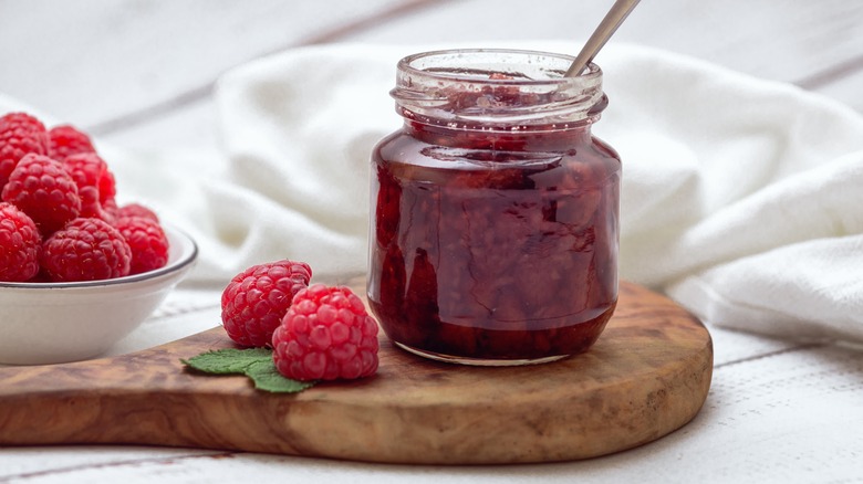 Raspberry jam in a glass jar with a spoon