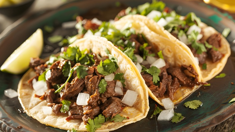 Three tacos de barbacoa with beef, onions, and cilantro