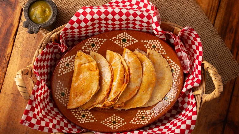 A basket of tacos de canasta with a side of salsa