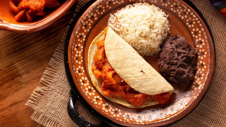 A taco de guisado on a plate with rice and refried beans