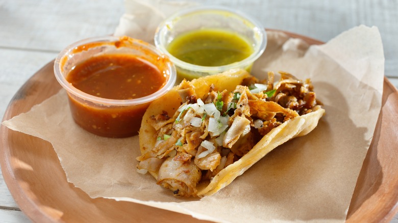 A taco de tripa on a plate with red and green salsa