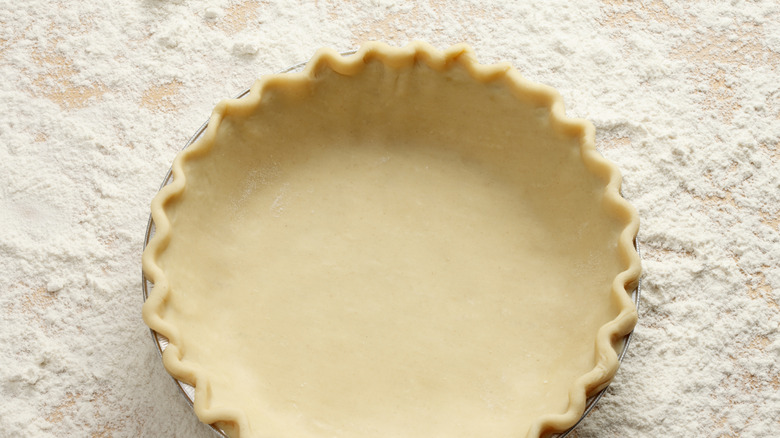 A neatly crimped pie crust sits on a floured table.