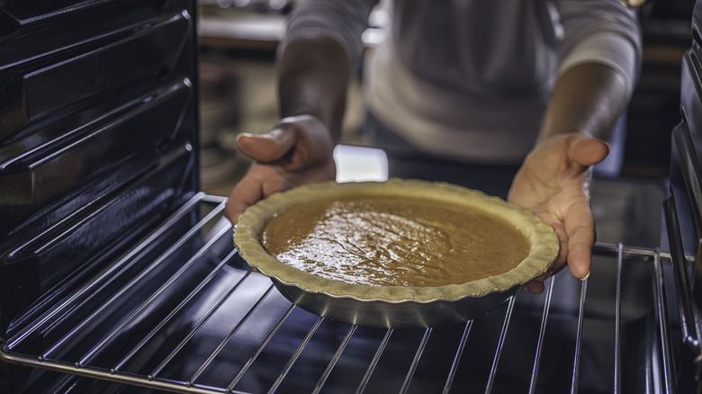 A person places a pumpkin pie in the oven.