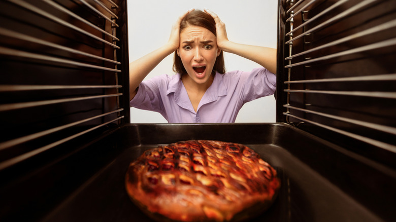 A woman looks at burnt pie in horror.