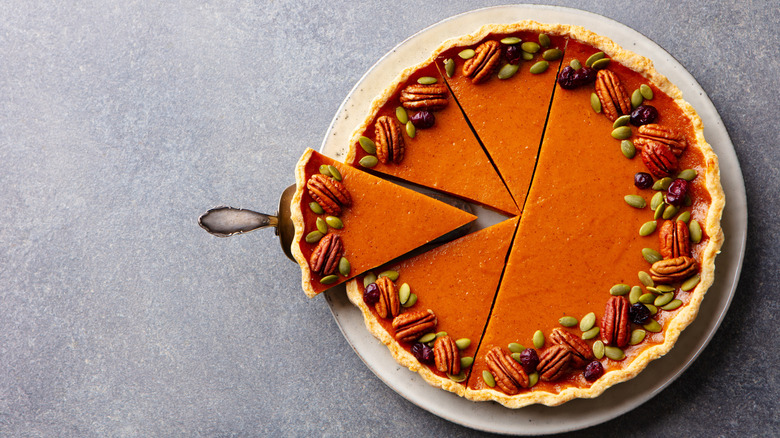 A sliced pumpkin pie is decorated with nuts and seeds.