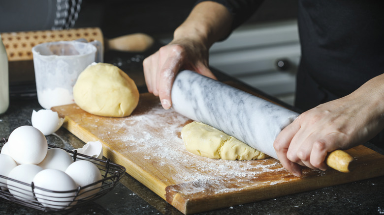 Hands are shown rolling out fresh pie dough.