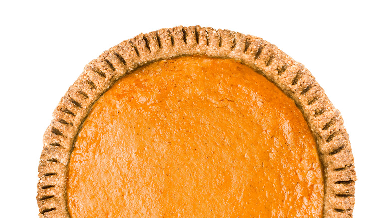 An aerial view shows a pumpkin pie with crimped edge on a white background.