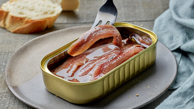 An open can of anchovies with a fork taking an anchovy out