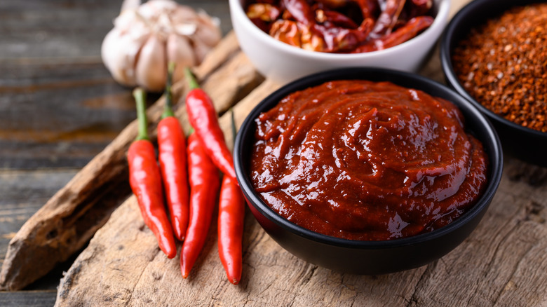 A dish of Gochujang chili sauce with chiles on a wooden table