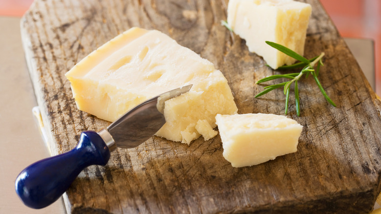 A wedge of cheddar cheese with a cheese knife on a wooden cutting board