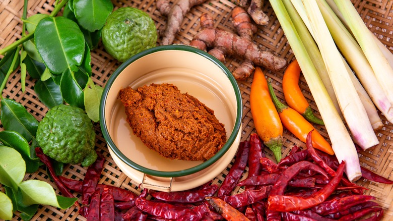 A dish of red curry paste on a counter with Asian ingredients like chiles, lemongrass, and limes