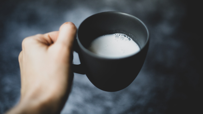 Hand holds mug of milk.