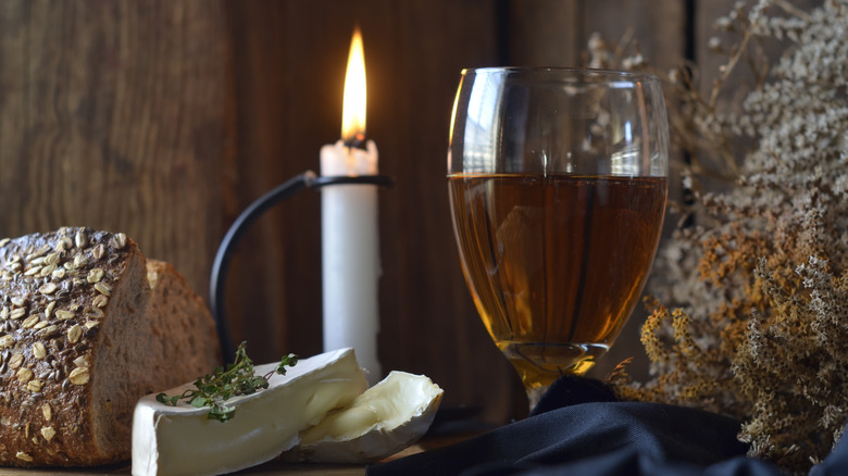 A glass of cider sits alongside a candle, bread, and cheese.