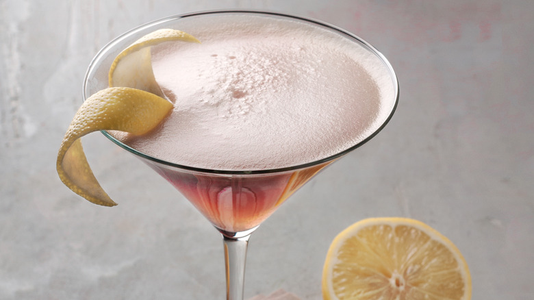 Cosmopolitan sits on a table next to half a lemon.